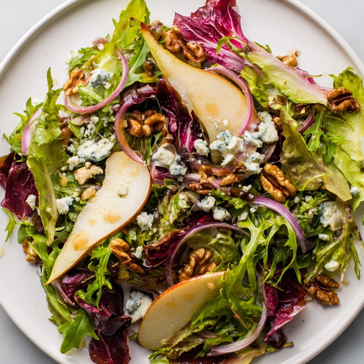 Vibrant bowl of Winter Green Salad with Pear and Candied Walnuts, finished with crunchy candied walnuts and sliced pear.