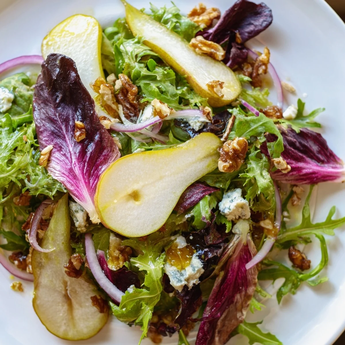 A plated Winter Green Salad with Pear and Candied Walnuts with blue cheese crumbles and red onion.
