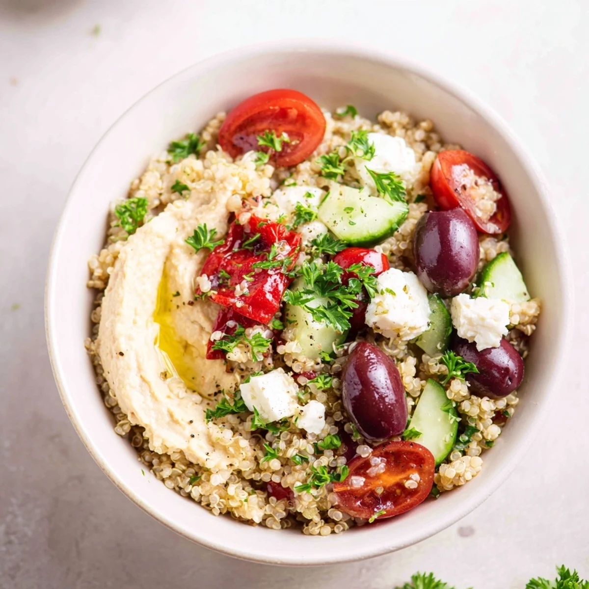 Spoon a generous dollop of creamy hummus over this Mediterranean Quinoa Bowl, garnished with colorful vegetables and briny Kalamata olives.