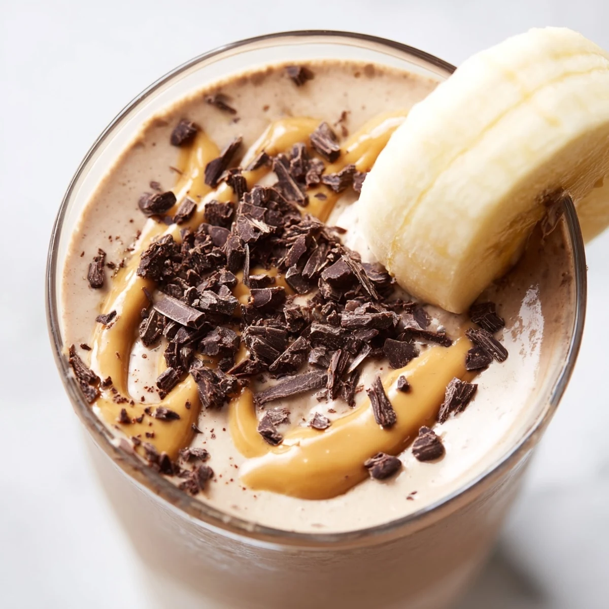 Close-up photo showing the thick, creamy texture of a Chocolate Peanut Butter Smoothie with Banana in a rustic glass beside fresh banana slices.