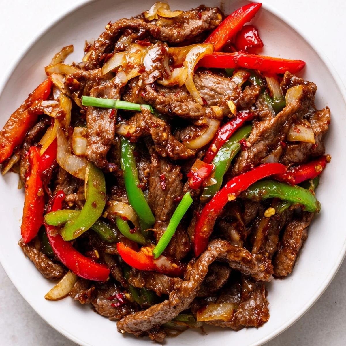 Close-up of a hot pan with sizzling strips of Spicy Stir Fry Beef tossed with crisp red and green bell peppers and onions in a glossy, spicy sauce, steam rising.