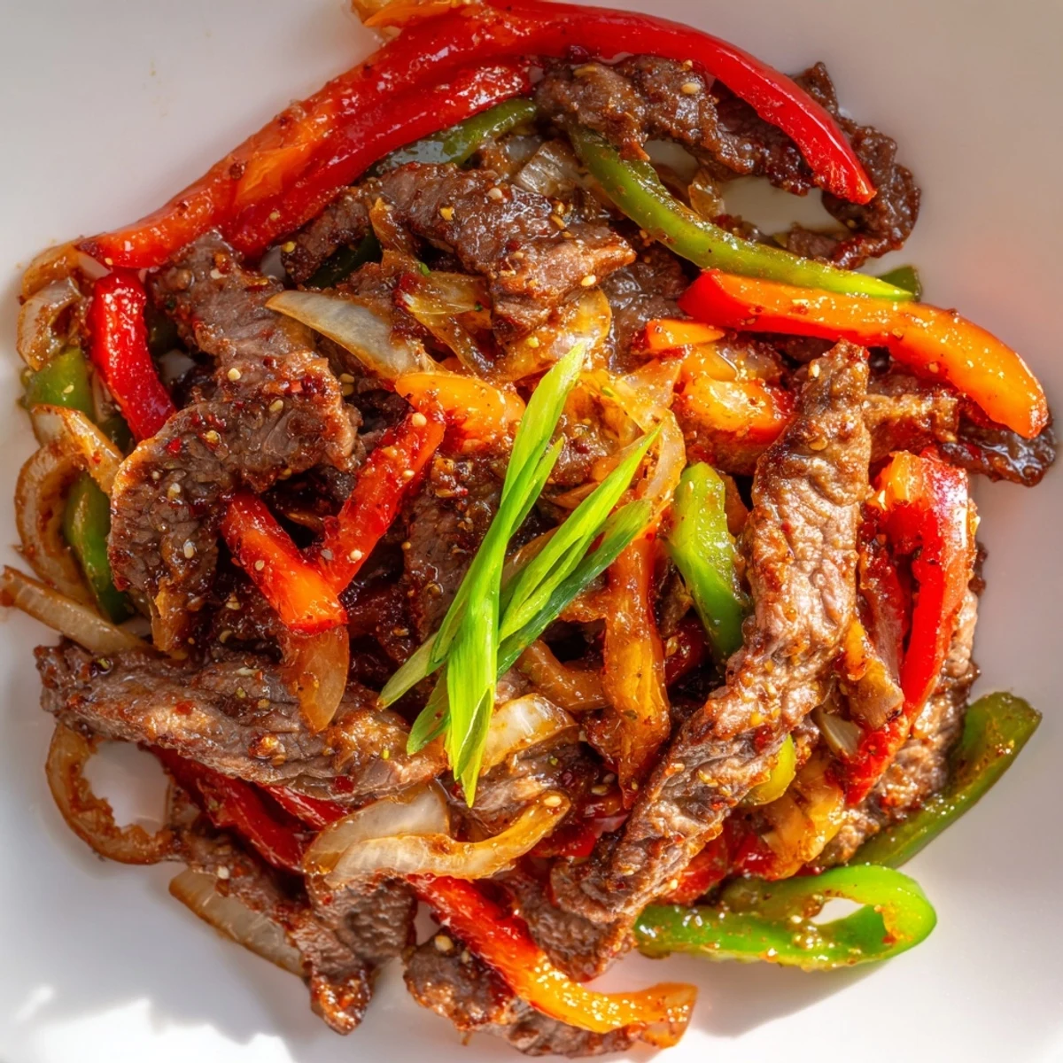 Freshly prepared Spicy Stir Fry Beef served in a white bowl over fluffy jasmine rice, garnished with sliced green onions and a spoonful of chili garlic sauce.