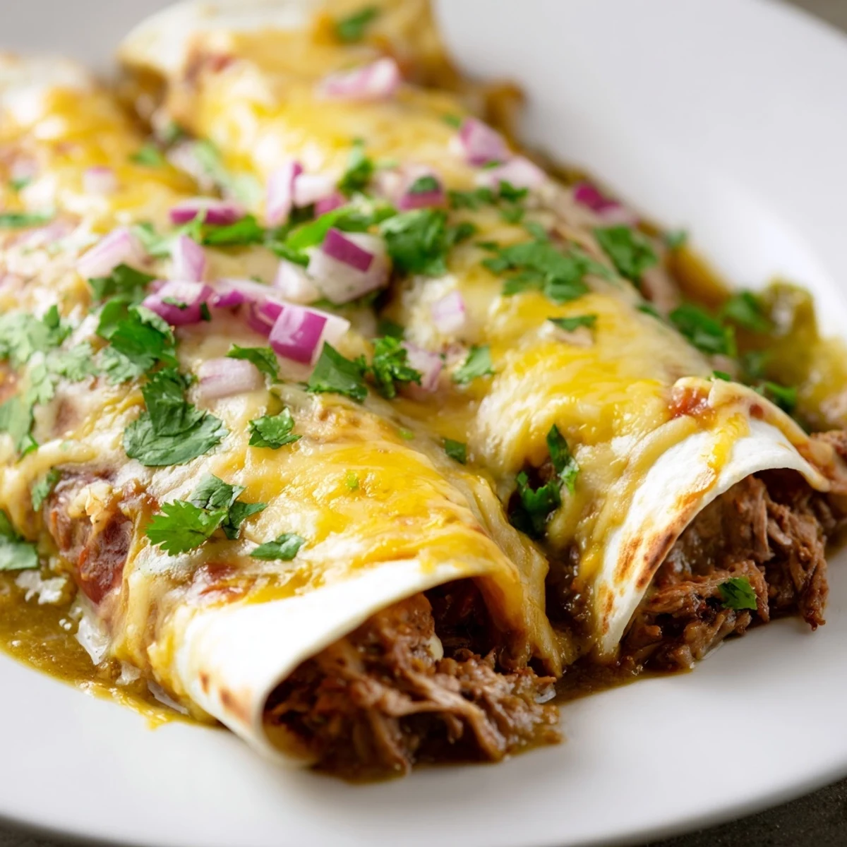Foil-covered baking dish of Beef Enchiladas with Green Chili Sauce, fresh from the oven with vibrant green toppings.