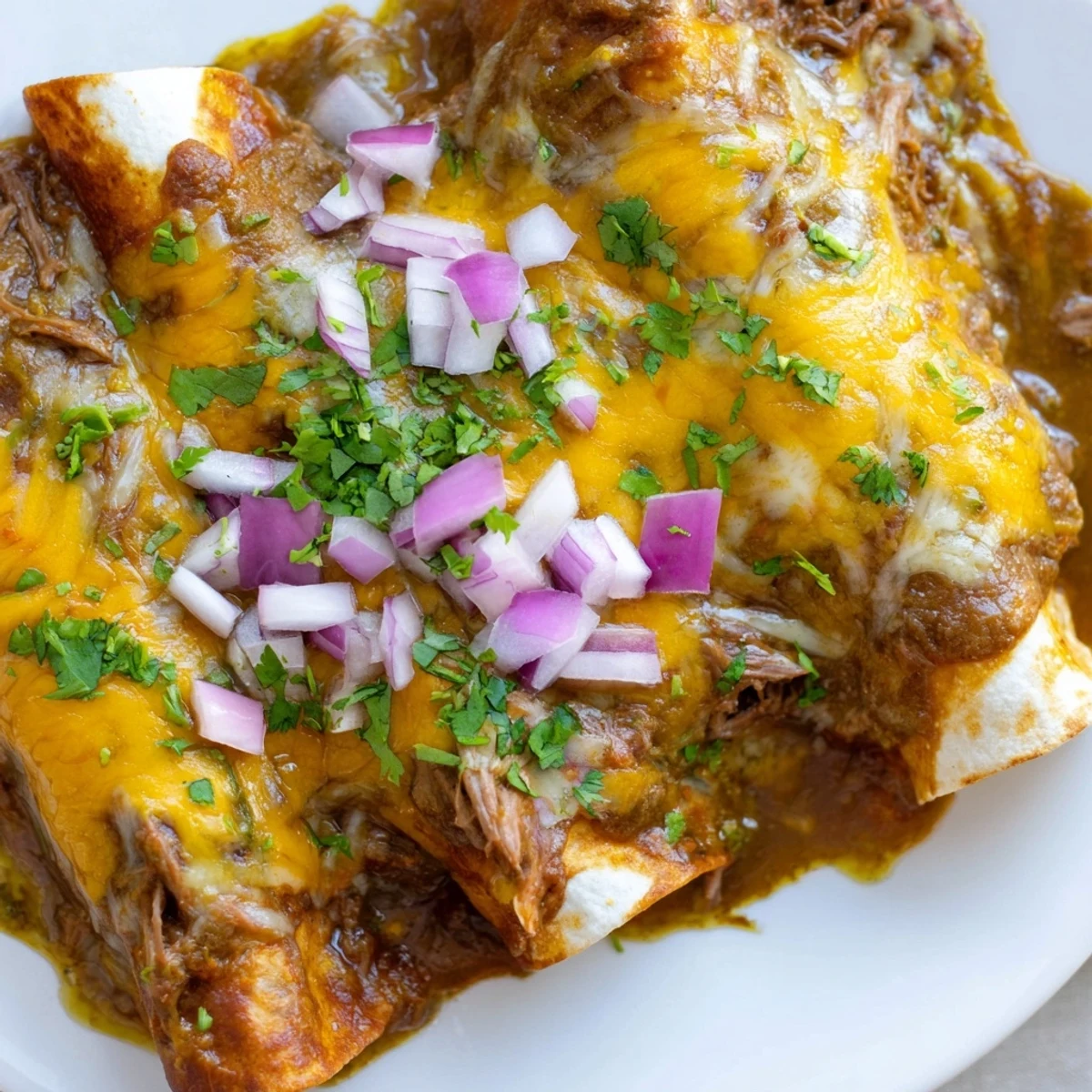 Tender shredded beef filling in Beef Enchiladas with Green Chili Sauce, garnished with cilantro and lime wedges.