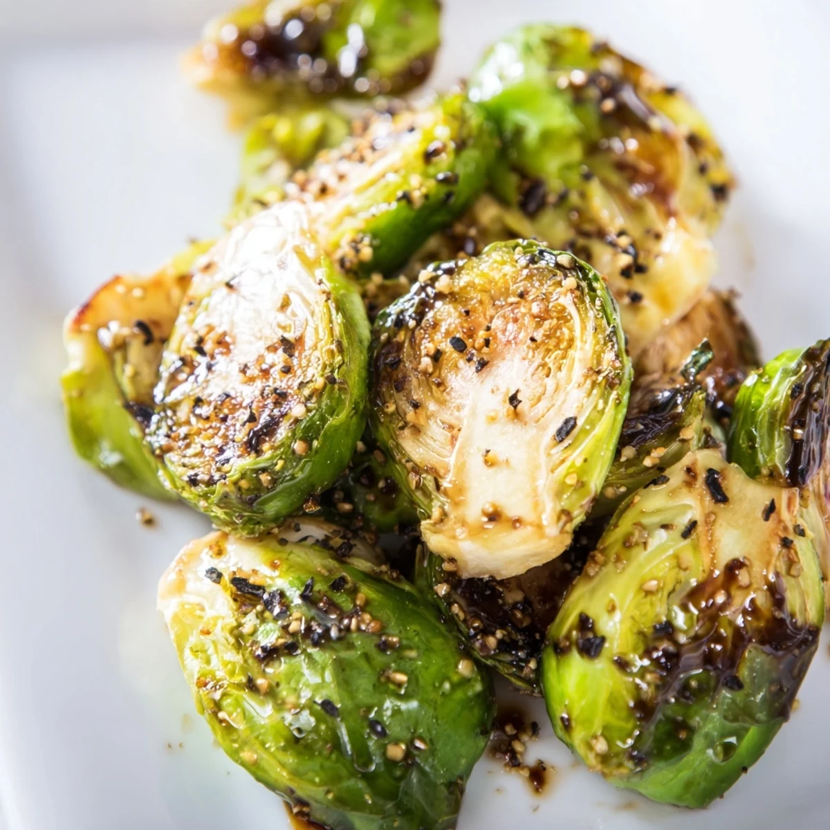 Shiny balsamic glaze coating freshly pulled Roasted Brussels Sprouts with Balsamic Glaze on a dark serving dish.