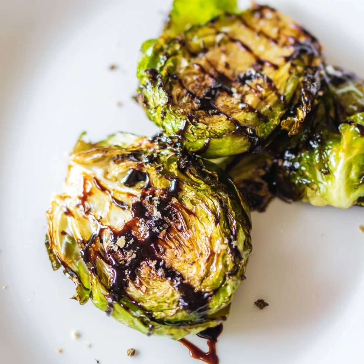 Halved Roasted Brussels Sprouts with Balsamic Glaze Reduction show crispy edges and a tangy-sweet glaze drizzle, topped with toasted pecans.
