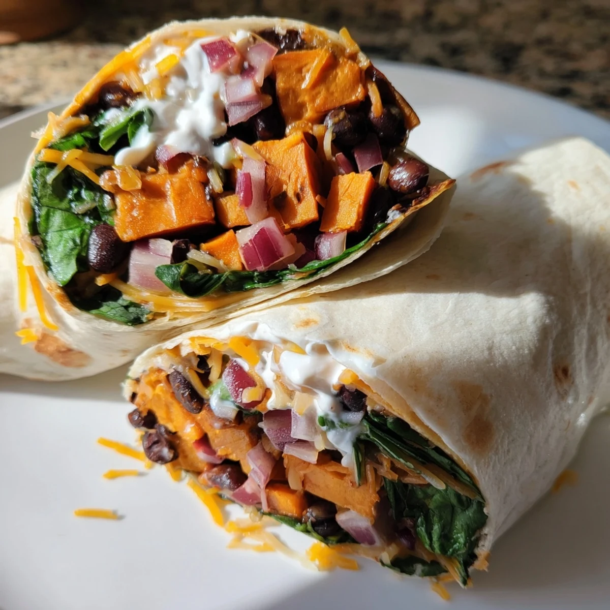 A hand holds a warm Roasted Sweet Potato and Black Bean Burrito, topped with fresh cilantro and a dollop of sour cream.