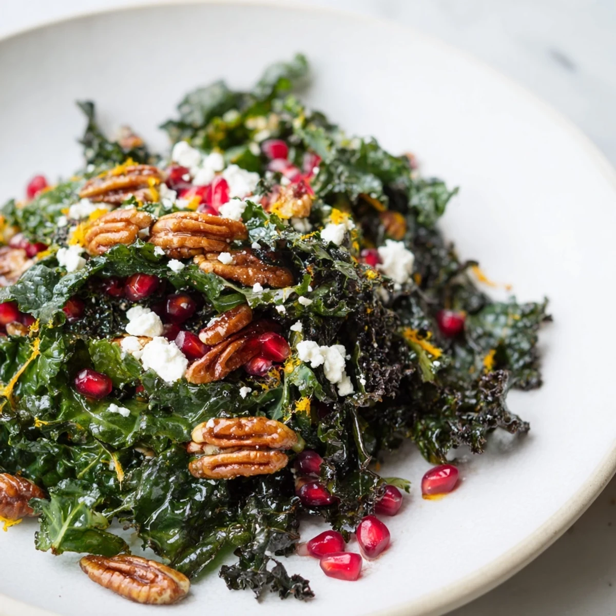 A freshly tossed Winter Kale Salad with Pomegranate and Pecans drizzled with citrus vinaigrette on a marble counter.