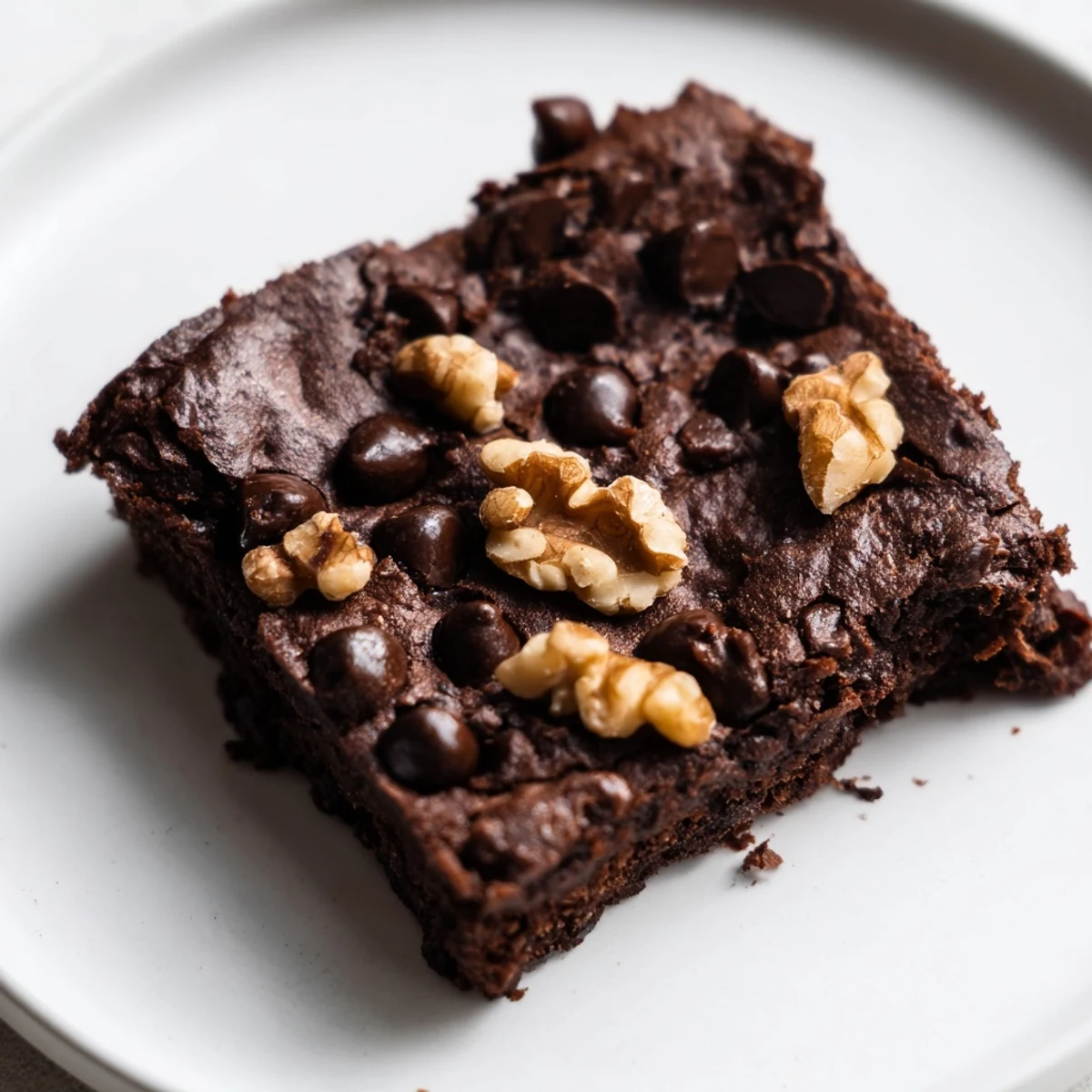 A close-up of warm chocolate fudge brownies with walnuts, showing a gooey center and crunchy nut pieces on a dark plate.