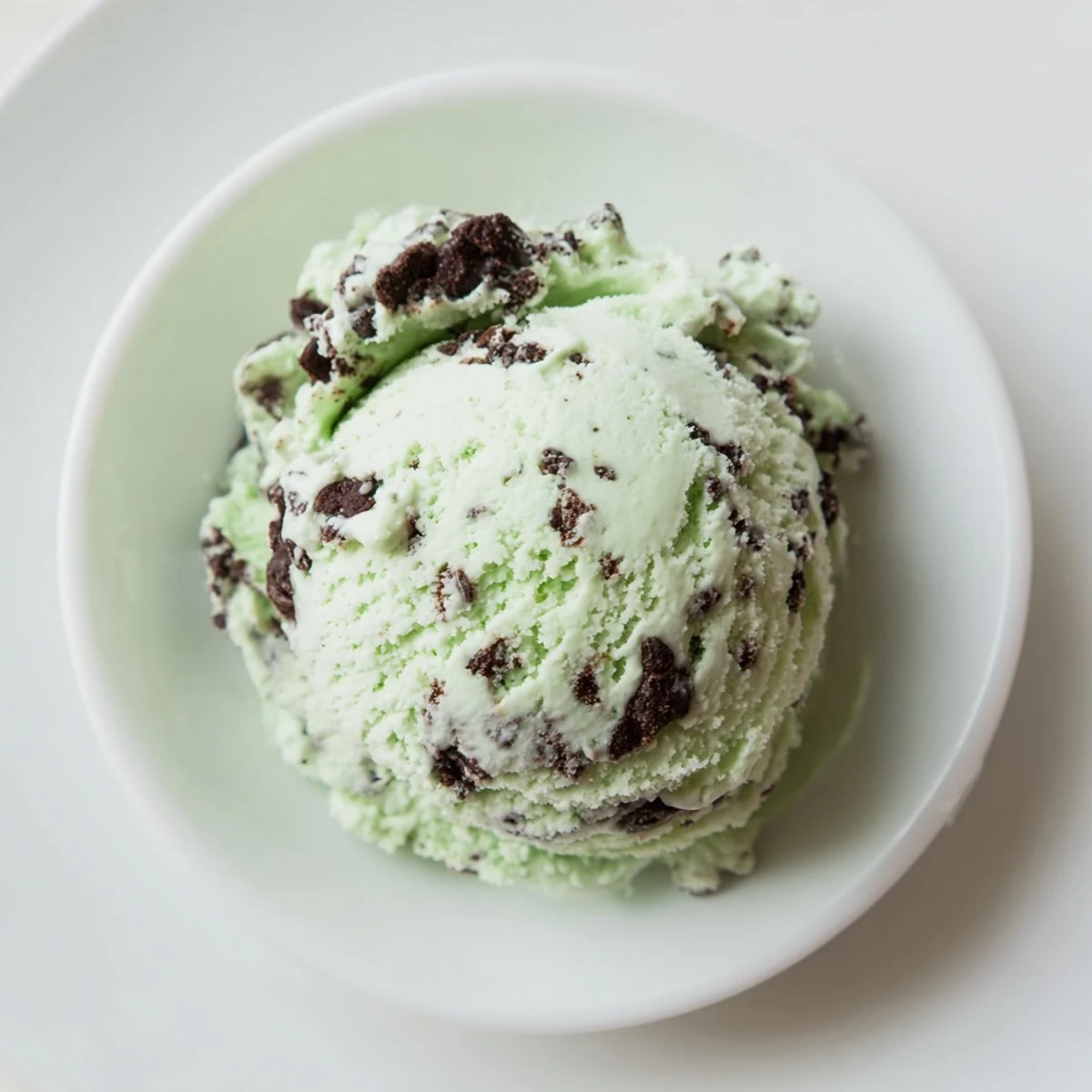 Close-up of homemade St. Patricks Day Mint Chocolate Chip Ice Cream scooped into a glass bowl, showcasing creamy mint green texture with rich chocolate chunks.