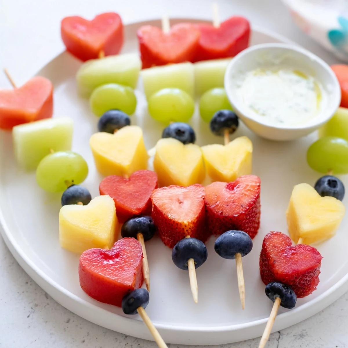Colorful Sweetheart Fruit Skewers with Yogurt Dip on a platter, featuring fresh strawberries, watermelon hearts, and grapes.