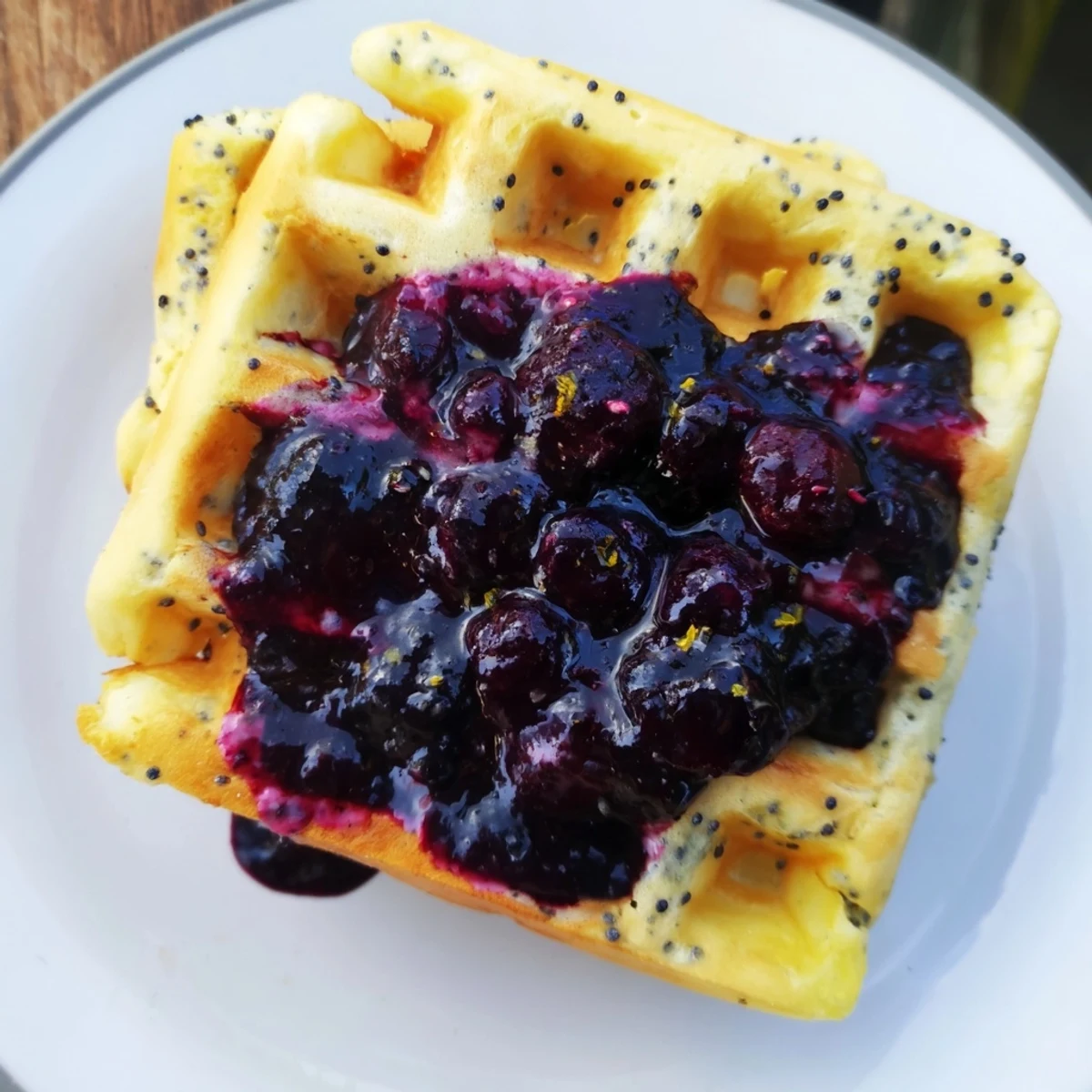 Golden Lemon Poppy Seed Waffles with blueberry syrup drizzled over the fluffy stack.