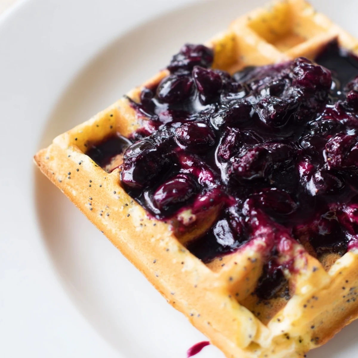 Light Lemon Poppy Seed Waffles served with blueberry syrup and a side of fruit.