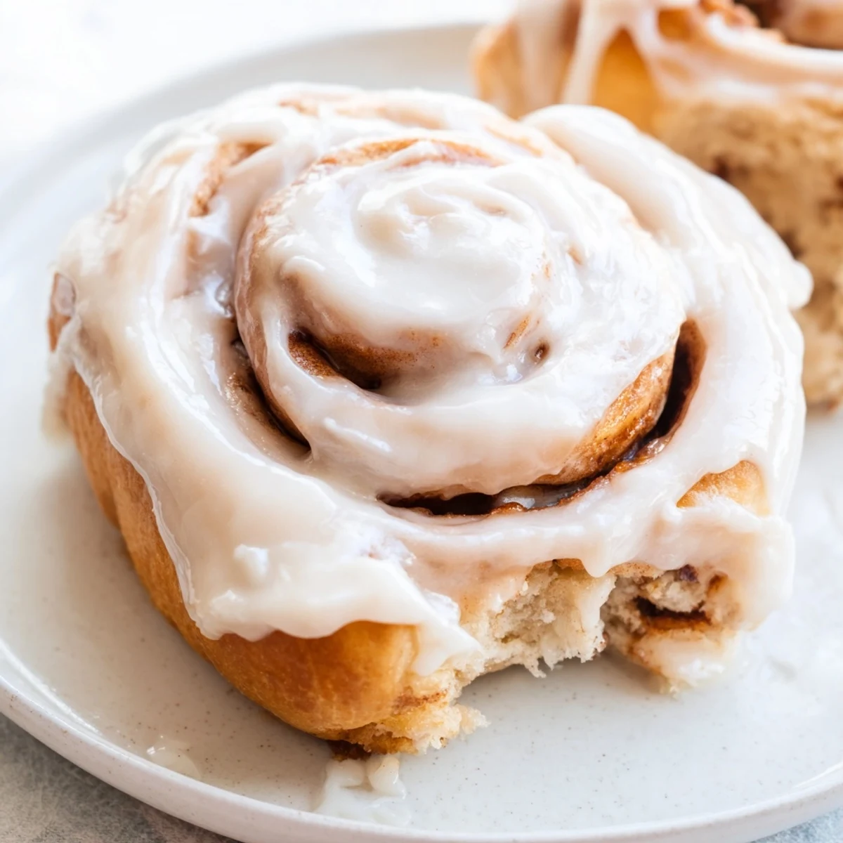 Freshly baked Keto Cinnamon Buns with cream cheese icing drizzled over warm, soft buns on a rustic wood surface.