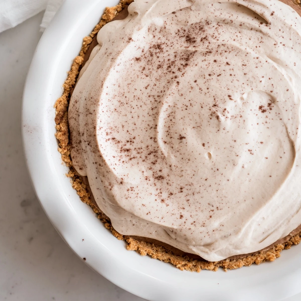 A slice of Keto Cold Brew Coffee Pie on a white plate, topped with whipped cream and a coffee bean garnish.