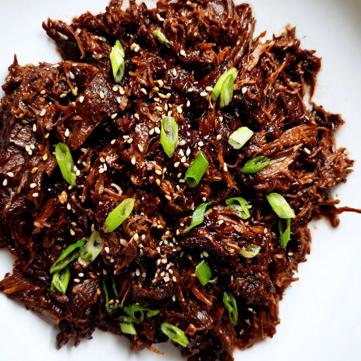 A close-up of Slow Cooker Korean Beef recipe shredded and garnished with green onions and chili slices.