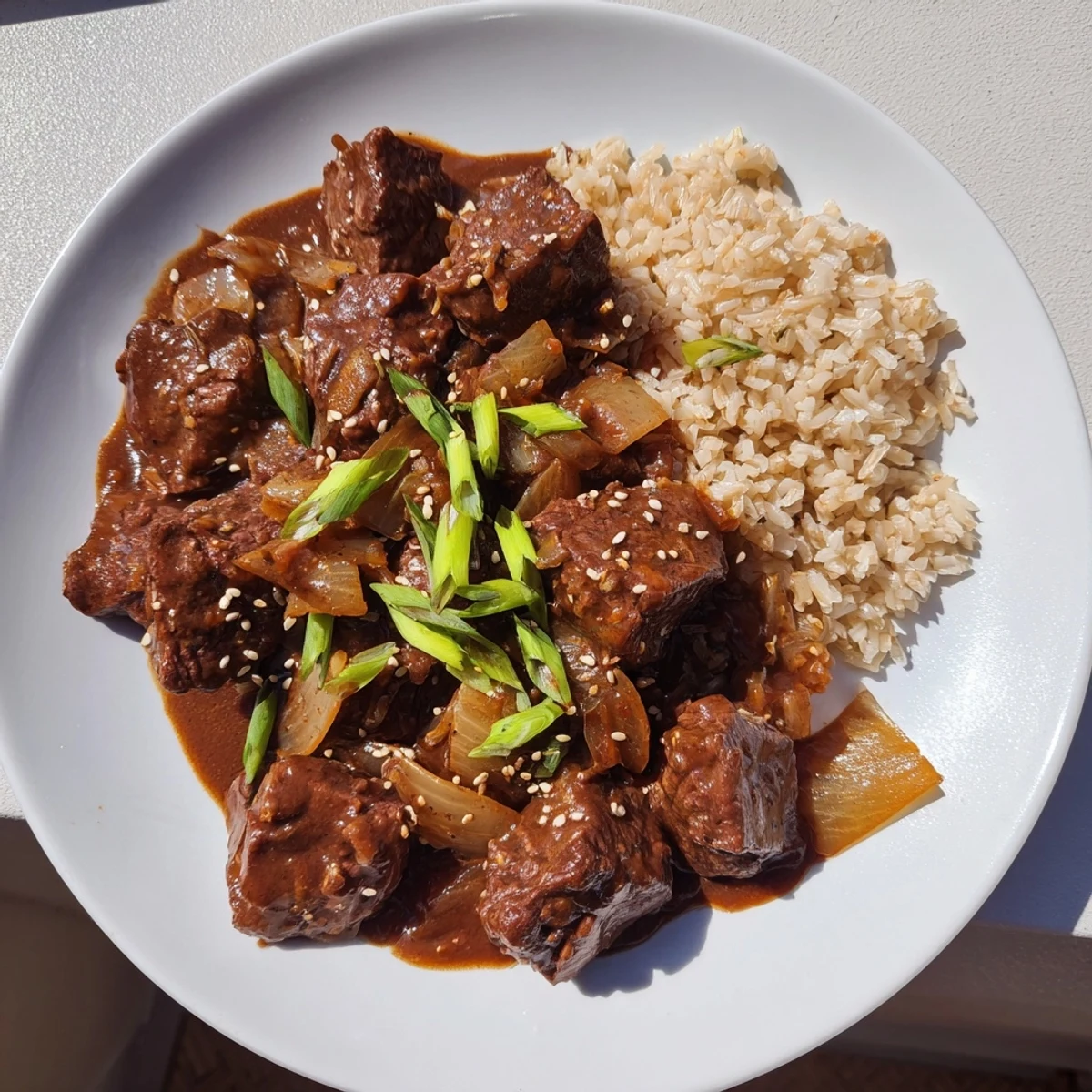 Tender chunks of Crock Pot Korean Beef simmering in a glossy, rich red sauce garnished with green onions and sesame seeds.