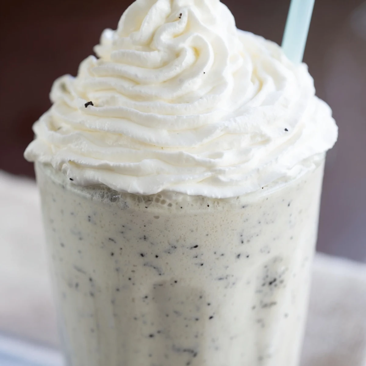 A creamy Vanilla Bean Frappuccino served with a straw beside fresh vanilla beans.