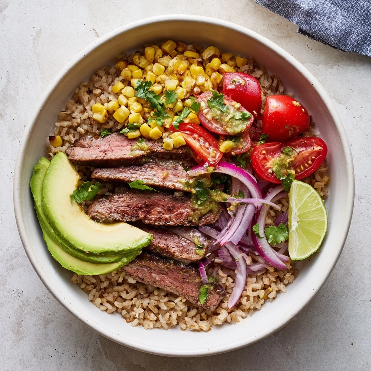 A close-up of a fresh Steak Avocado Roasted Corn Bowl showing golden roasted corn, diced tomatoes, red onion, and a drizzle of zesty lime dressing.