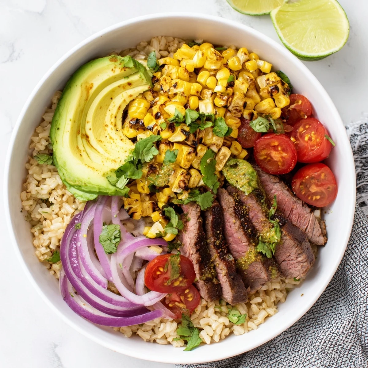 Overhead view of a colorful Steak Avocado Roasted Corn Bowl with sliced steak, avocado, cilantro, and lime wedges ready for a satisfying lunch or dinner.