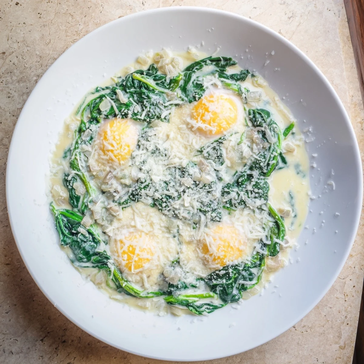 A close view of Creamy Spinach and Eggs, featuring velvety Parmesan sauce and runny yolks, served with crusty bread.