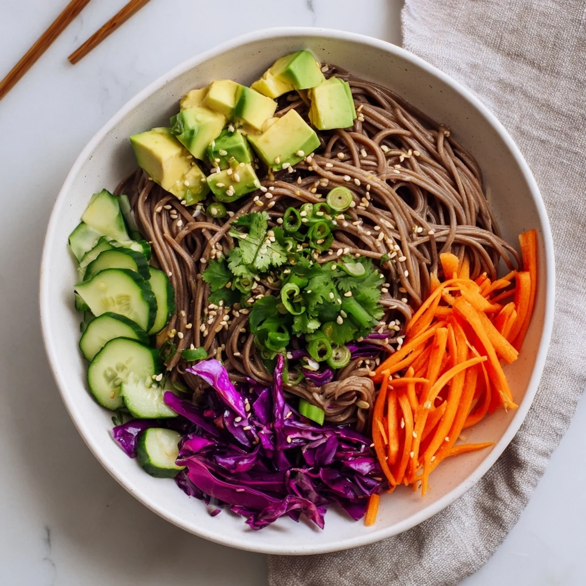 A close-up of Sesame Avocado and Soba Noodle Salad garnished with green onions and sesame seeds, glistening with savory dressing.