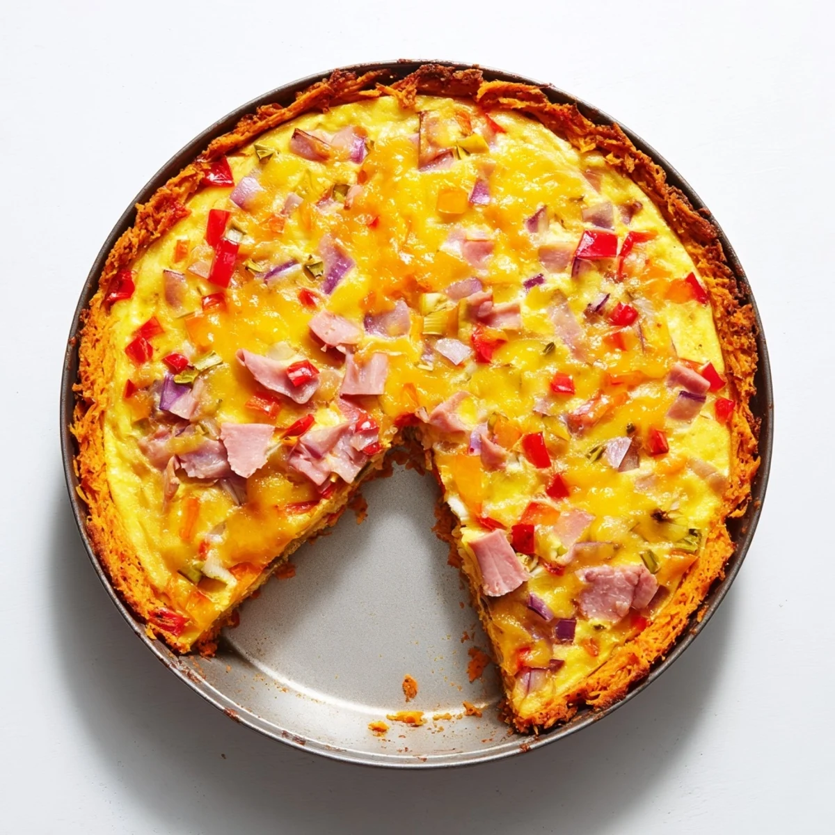 Overhead view of the Red Capsicum and Ham Quiche with Sweet Potato Crust reveals the bubbly cheese topping and colorful diced ham and red peppers inside the flaky crust.