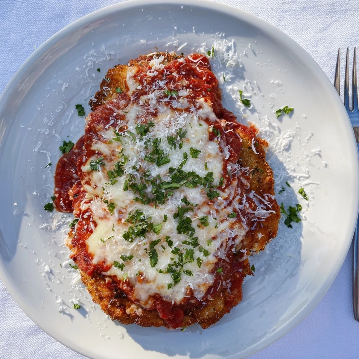 Serving Chicken Parmigiana over spaghetti with fresh basil garnish and melted cheese on crispy chicken breasts.