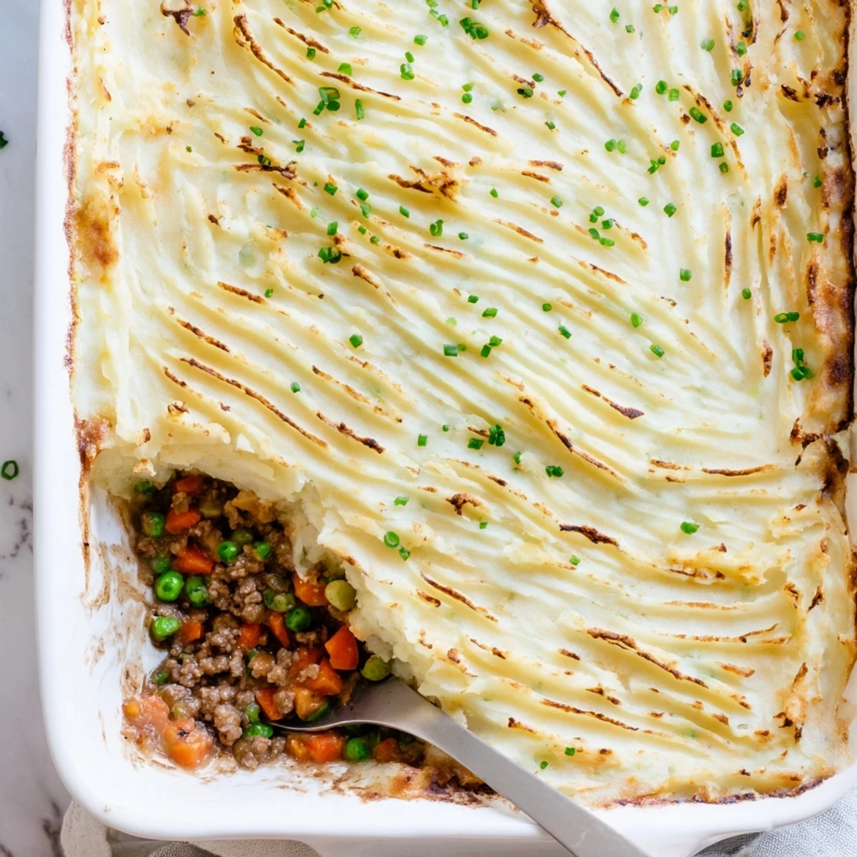 Steaming Shepherds Pie with Creamy Garlic Mashed Potatoes reveals swirls of buttery potatoes over rich meat and vegetables on a rustic serving dish.