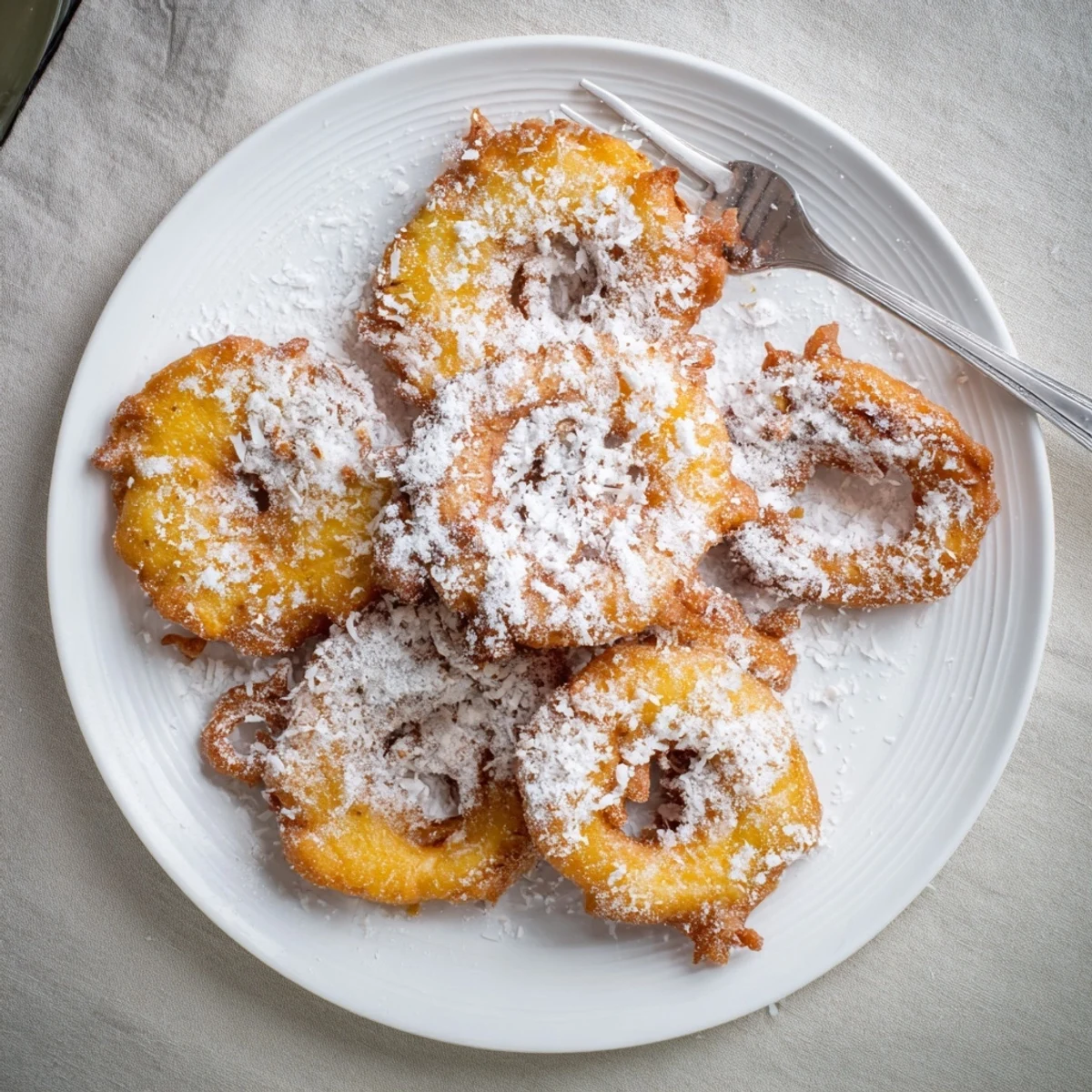 Golden Heavenly Pineapple Fritters That Bring Tropical Joy arranged on a white plate, dusted with powdered sugar and toasted coconut.