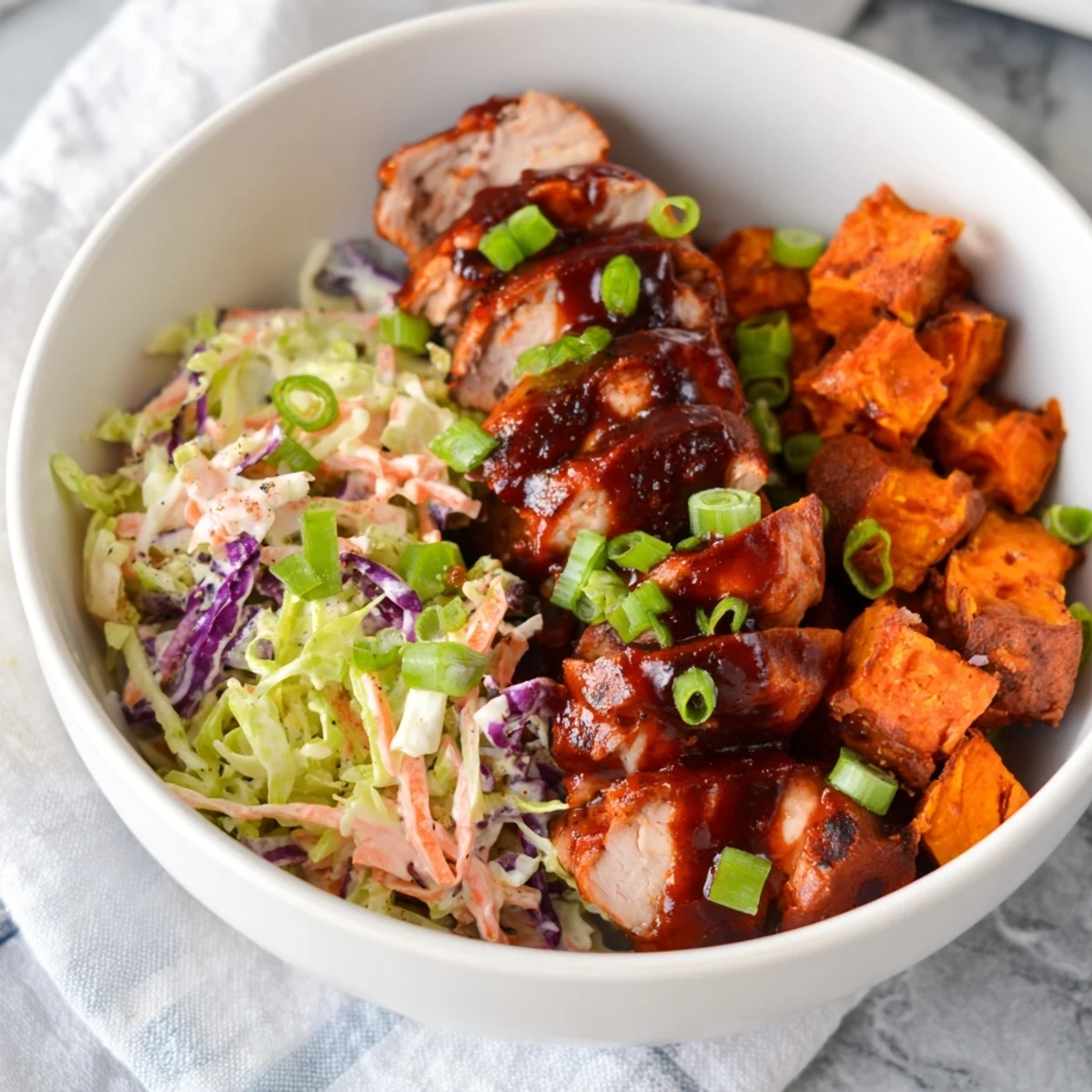 Hearty BBQ chicken bowl with roasted sweet potatoes and colorful coleslaw garnished with fresh cilantro and lime