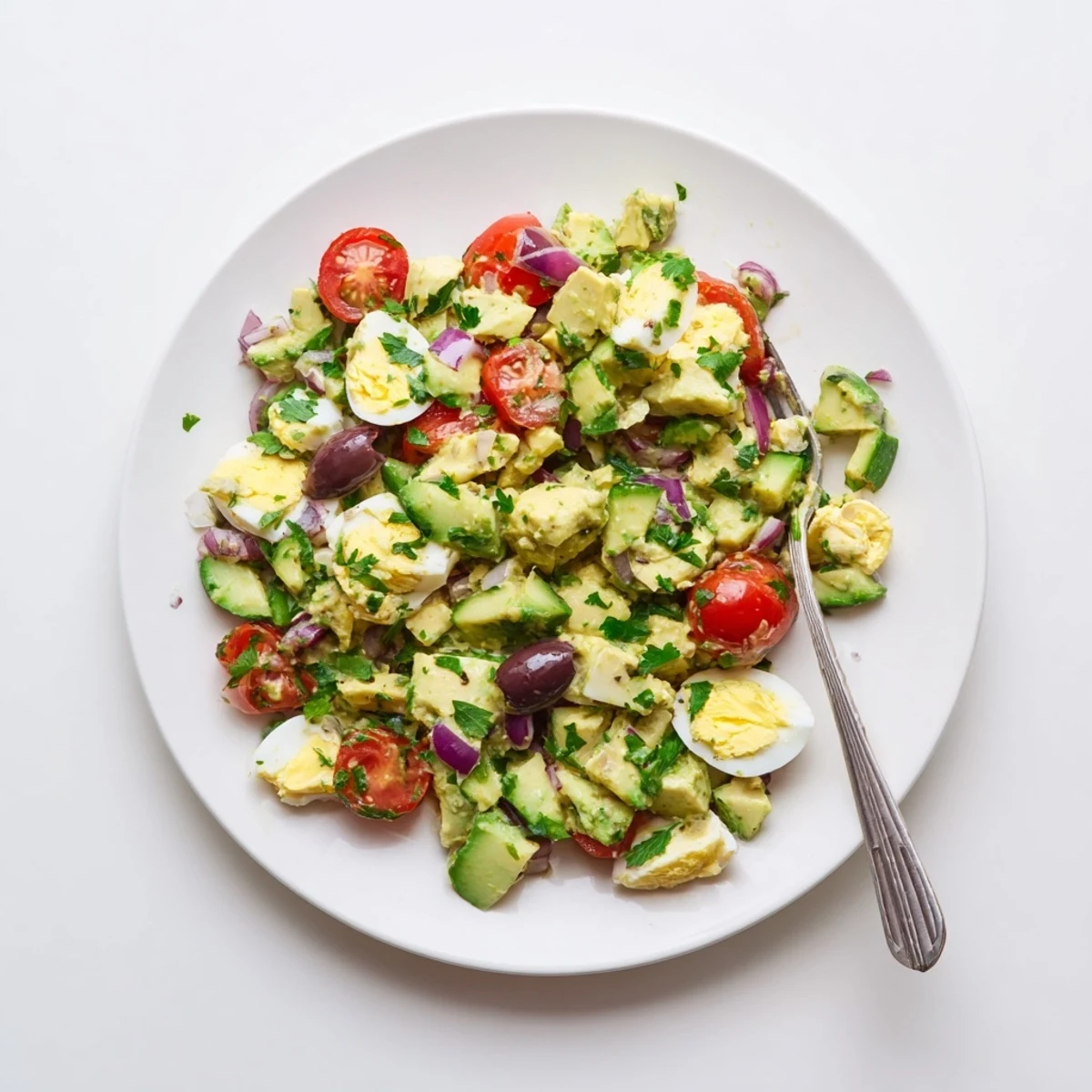 Creamy Mediterranean avocado egg salad featuring diced avocados, chopped eggs, cherry tomatoes, Kalamata olives, and fresh parsley in a lemon olive oil dressing