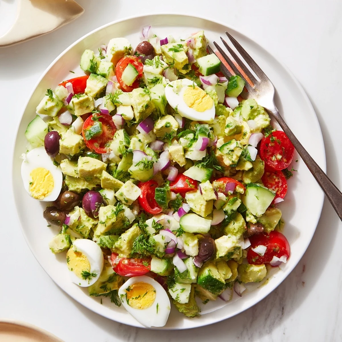 Colorful bowl of zesty avocado egg salad loaded with crisp cucumber, red onion, tomatoes, and olives drizzled with tangy lemon garlic vinaigrette