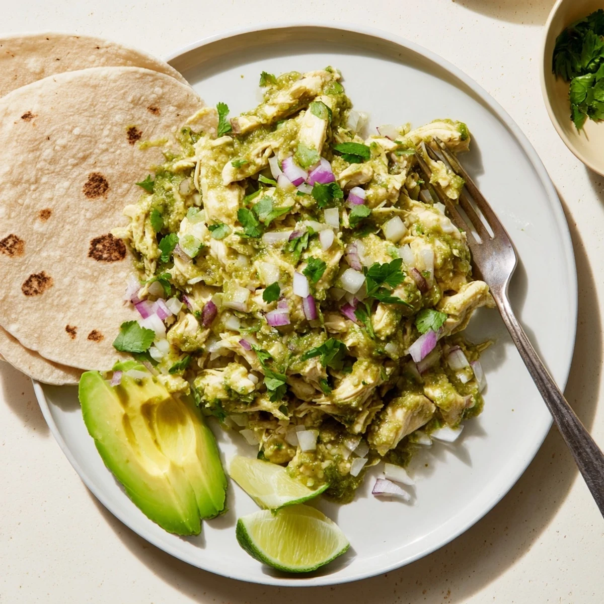 Tender shredded chicken coated in zesty salsa verde sauce, garnished with fresh cilantro and lime.