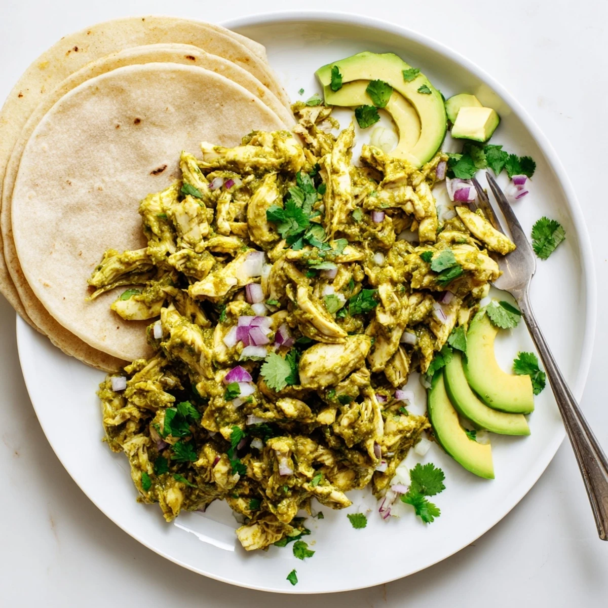 Salsa Verde Chicken with creamy avocado slices, red onion, and cilantro for a colorful taco dinner.