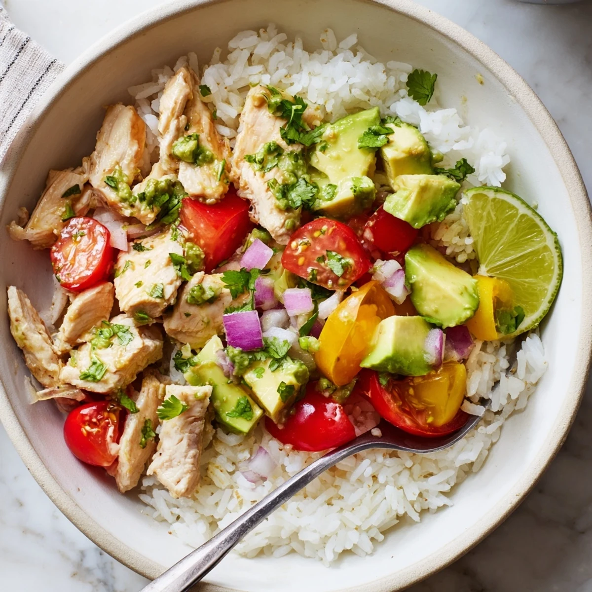 Colorful rice bowl featuring marinated honey lime chicken pieces alongside ripe avocado and bright lime wedges