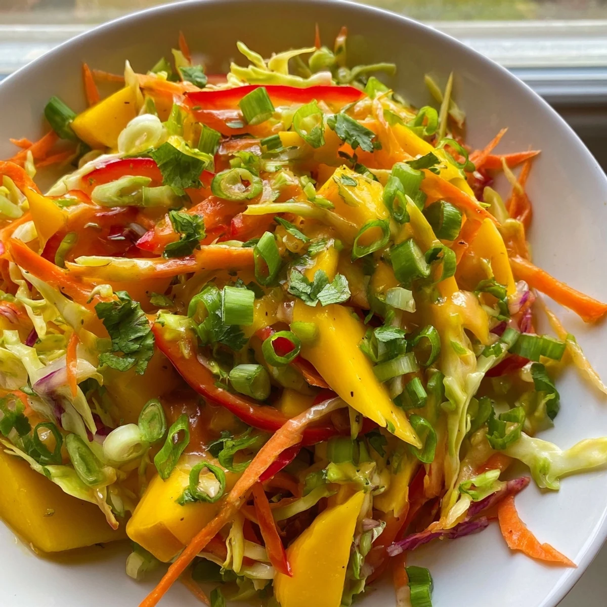 Fresh vibrant mango slaw with colorful shredded vegetables and zesty lime dressing in a white bowl