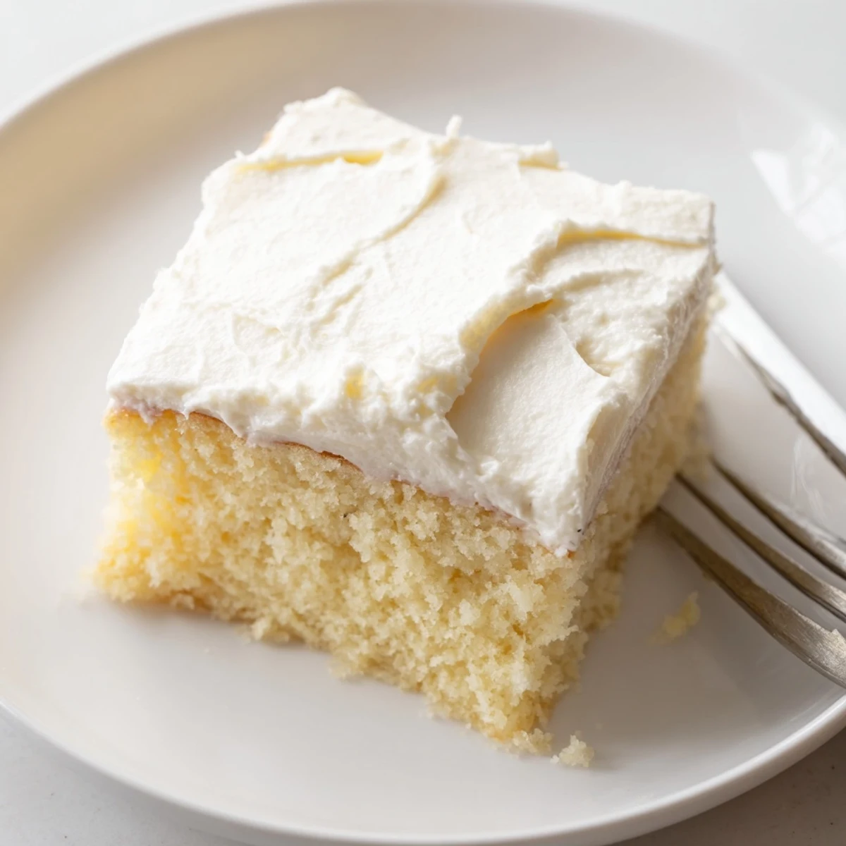 Golden vanilla church cake slice with fluffy white frosting on a vintage floral plate