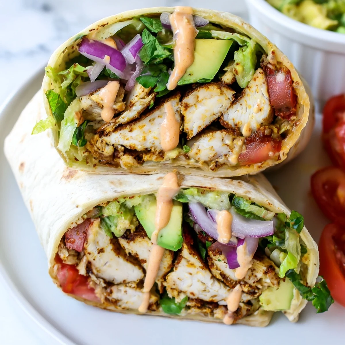 Close-up of spicy chicken avocado wraps cut in half showing layers of protein, vegetables, and zesty condiments inside