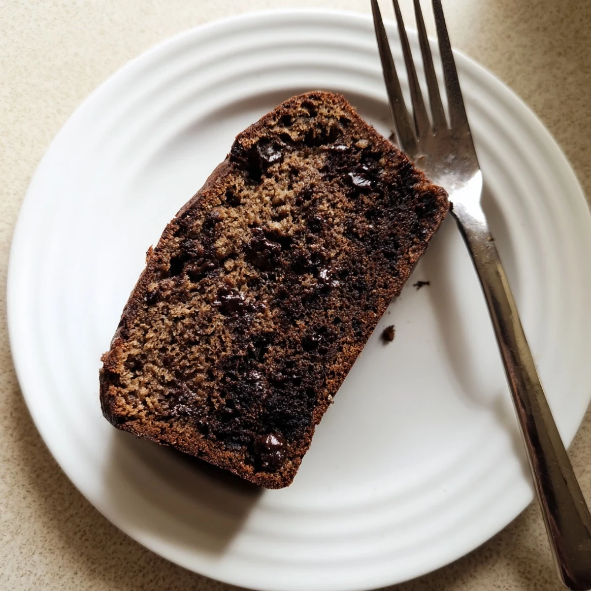 Warm slice of chocolate espresso banana bread topped with melting butter on a white plate