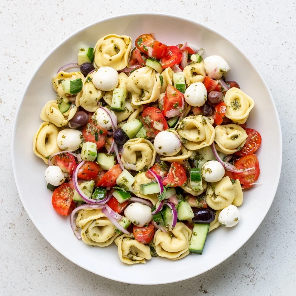 Colorful tortellini pasta salad with cherry tomatoes, cucumber, and mozzarella in a zesty Italian herb dressing