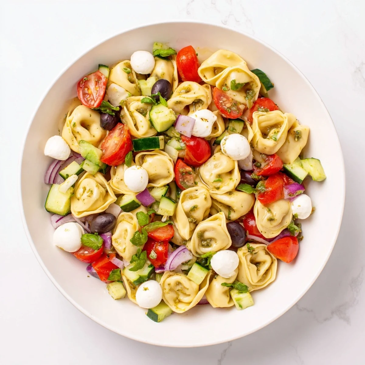 Cheese-filled tortellini pasta salad tossed with crisp vegetables and basil, served chilled in a white bowl