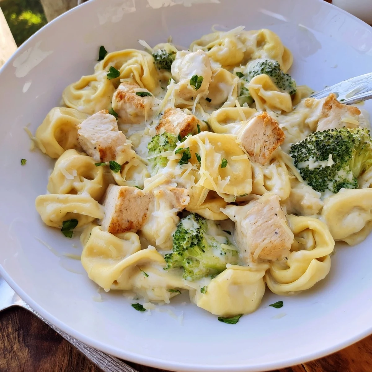 Steaming plate of Creamy Garlic Parmesan Tortellini Chicken Broccoli Recipe, garnished with parsley