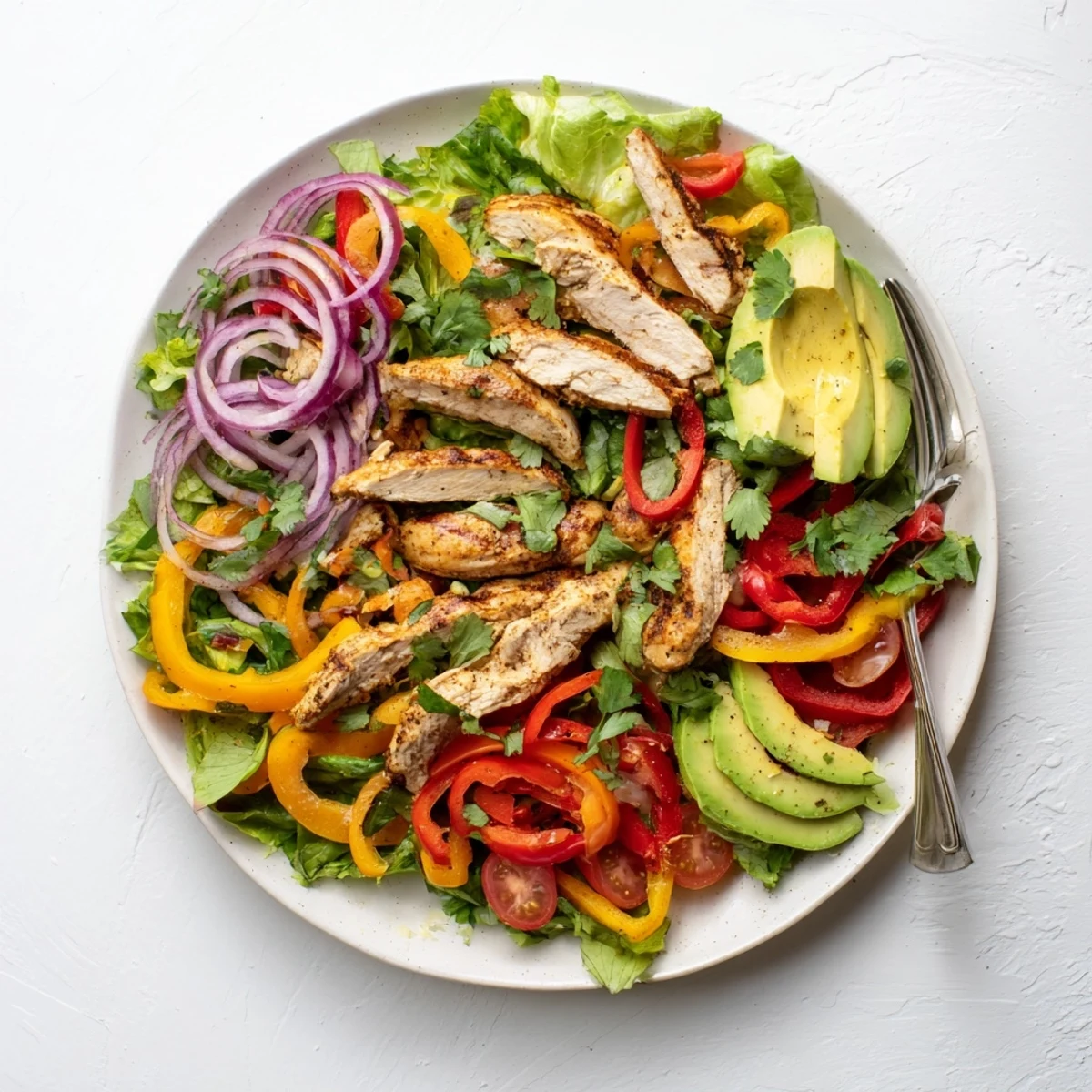 Healthy grilled chicken fajita salad featuring spiced chicken strips over mixed greens with cherry tomatoes and red onion.