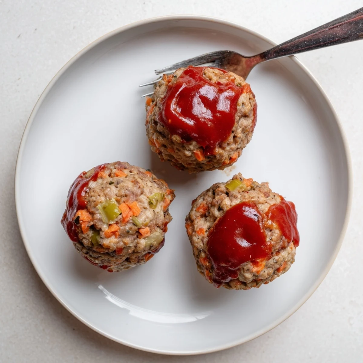 Individual portion-sized turkey meatloaf muffins baked with vegetables and herbs on a white plate
