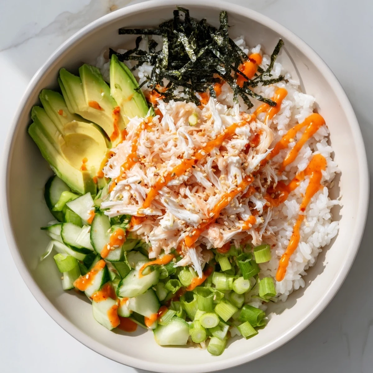 Deconstructed California roll sushi bowl topped with fresh avocado, crab, cucumber, and spicy mayo drizzle