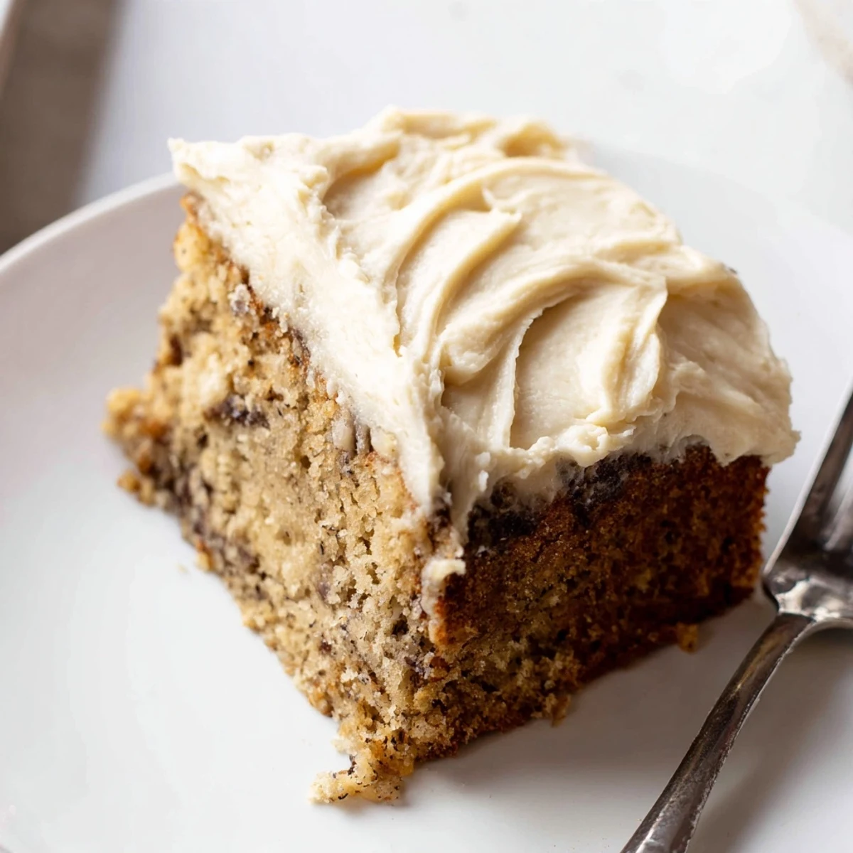 Moist Brown Butter Banana Cake topped with swirls of tangy cream cheese frosting served on a ceramic plate