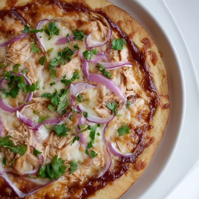 BBQ chicken pizza with red onion and cilantro, sliced on a rustic cutting board.