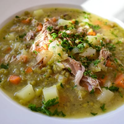 Hearty Green Split Pea Soup with Smoked Turkey Leg simmering in a pot, featuring diced carrots and celery in the rich broth.