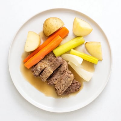 Close-up of Slow Cooker Beef Pot Roast with Root Vegetables beside a rustic loaf, with steam rising from the savory broth.